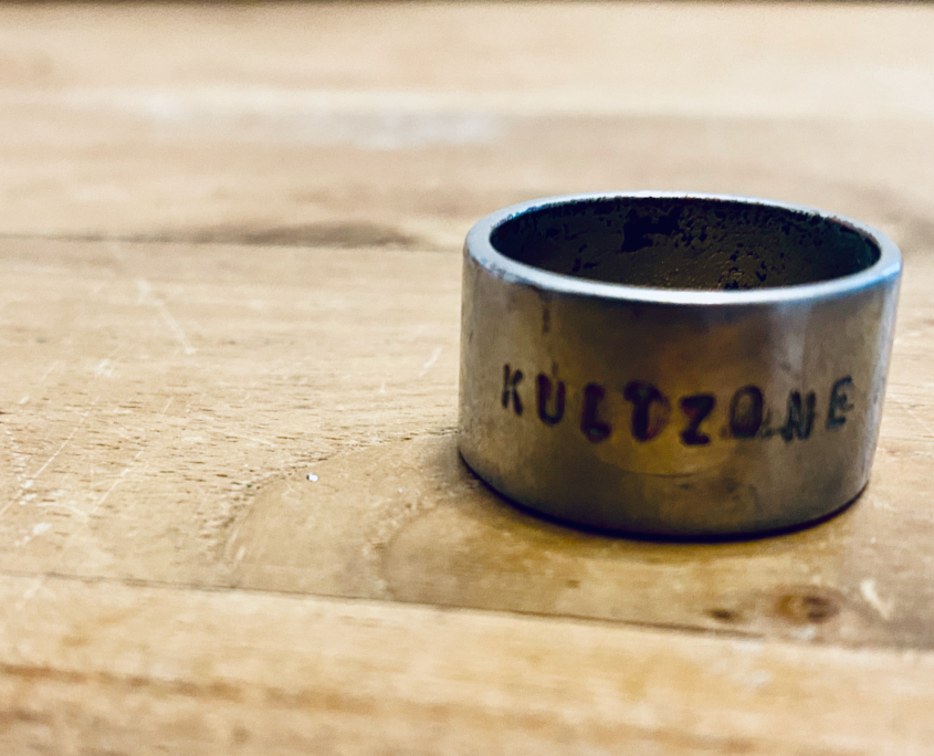 Kultzone - Symbolfoto (Ring mit Kultzone-Gravur auf Holzbrett)